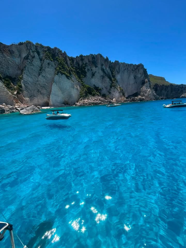 Brilliant blue water and white cliffs on the south coast of Zakynthos, small boats anchored close in